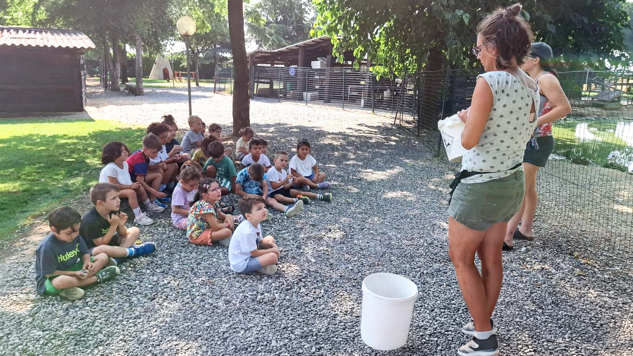 Bambini seduti all&rsquo;aperto ascoltano un&rsquo;educatrice durante un&rsquo;attivit&agrave; del centro estivo Haiku.