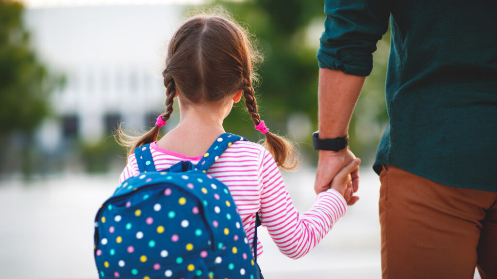 Bambina con lo zaino tiene per mano un adulto durante il rientro a scuola.